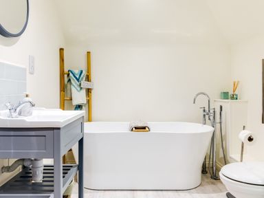 A bathroom with a freestanding bathtub a gray sink unit a toilet and a wooden ladder with towels at Goose Cottage - within the Helland Barton Farm collection in Delabole