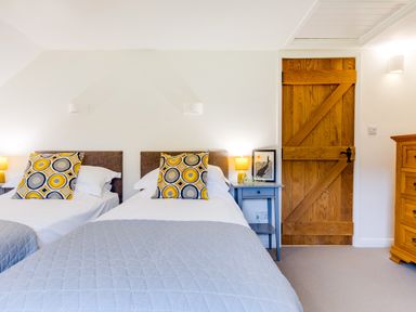 A bedroom with two single beds a wooden door a blue bedside table with a lamp and a framed picture at Goose Cottage within the Helland Barton Farm collection in Delabole