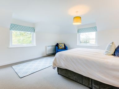 A bedroom with a bed two windows a blue armchair and a rug at Goose Cottage within the Helland Barton Farm collection in Delabole