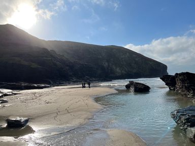 A beach with rocks water and cliffs under a blue sky with people standing on the sand at Goose Cottage - within the Helland Barton Farm collection in Delabole