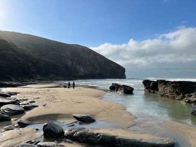 A sandy beach with rocks and people standing near the ocean at Goose Cottage within the Helland Barton Farm collection in Delabole