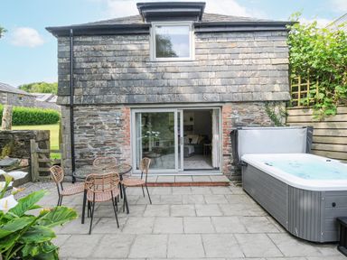 An outdoor patio with a round table and four chairs next to a hot tub outside a stone cottage with sliding glass doors Goose Cottage - within the Helland Barton Farm collection Delabole