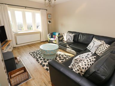 A living room with a black leather sofa and polka dot cushions a round patterned coffee table and a multicolor armchair at Sandtop in Tenby