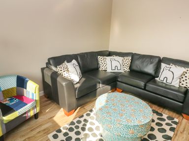 A corner with a black leather sectional sofa with patterned cushions a colorful patchwork armchair and a round patterned ottoman on a polka dot rug at Sandtop in Tenby