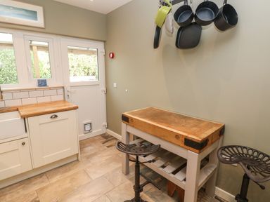 A kitchen area with a wooden countertop sink a door with windows hanging pots and pans a butcher block counter and two stools at Sandtop in Tenby