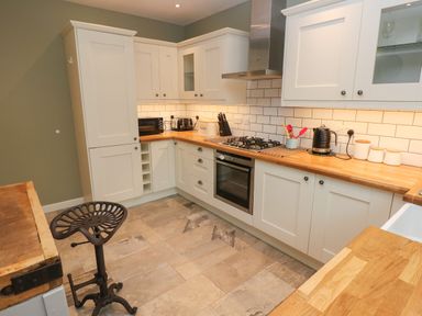 A kitchen with white cabinets wooden countertops a gas stove oven a black stool and various kitchen appliances at Sandtop in Tenby