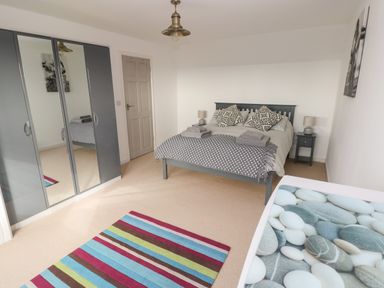 A bedroom with a double bed two bedside tables a striped rug and mirrored wardrobes at Sandtop in Tenby