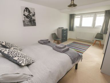 A bedroom with a bed pillows and folded towels next to two chairs a chest of drawers and a striped rug at Sandtop in Tenby