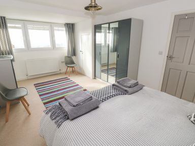 A bedroom with a striped rug two chairs a wardrobe with mirrored doors and a bed with towels at Sandtop in Tenby