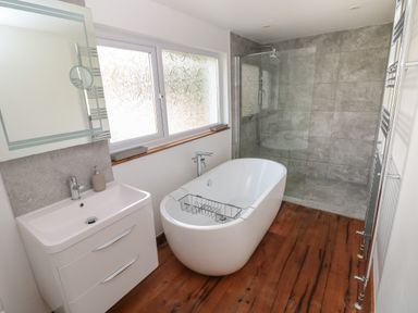 A bathroom with a freestanding bathtub a sink with cabinet a glass shower area and wooden floor at Sandtop in Tenby