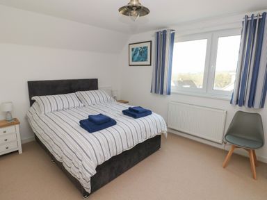 A bedroom with a bed with striped bedding towels on the bed a chair beside a window with striped curtains and a bedside table with a lamp at Sandtop in Tenby