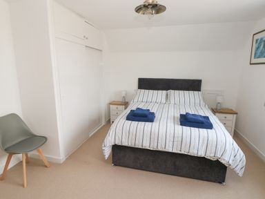 A bedroom with a bed that has striped bedding and blue towels on it a gray chair and white wardrobes at Sandtop in Tenby