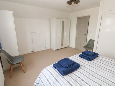 A bedroom with a bed with striped bedding and folded towels two gray chairs two white wardrobes and a gray door at Sandtop in Tenby