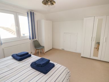 A bedroom with a bed with folded blue towels a gray chair two white wardrobes and windows with blue striped curtains at Sandtop in Tenby