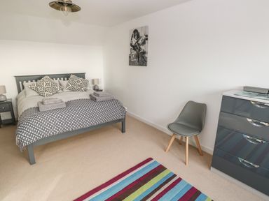 A bedroom with a bed with patterned pillows two nightstands a gray chair a gray dresser and a striped rug at Sandtop in Tenby