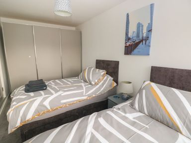 A bedroom with two single beds with patterned bedding a bedside table with a lamp and a large wardrobe at Sandtop in Tenby