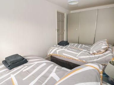 A bedroom with two single beds each with towels on top and a large wardrobe in the corner at Sandtop in Tenby