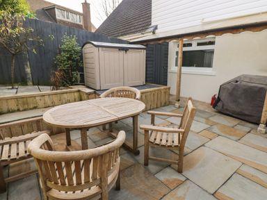 An outdoor patio with a wooden table and chairs a storage shed and a covered barbecue at Sandtop in Tenby