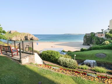 A beach with sand sea and rocks viewed from a garden with flowers benches and a gate at Sandtop in Tenby