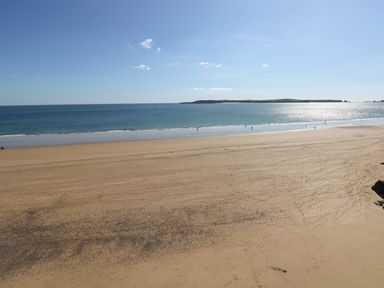 A wide sandy beach with footprints and a few people near the water at Sandtop in Tenby