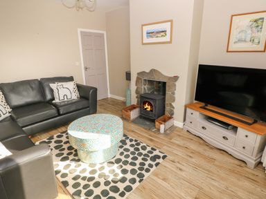 A living room with black sofas a round patterned ottoman a fireplace and a television on a cabinet at Sandtop in Tenby