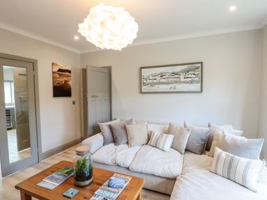 A living room with a sofa and cushions a wooden table with a glass jar and magazines and wall paintings at 41 Chatsworth Gardens Scarborough