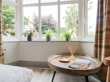A corner of a room with large windows a round wooden coffee table three potted plants on the window sill and checked curtains at 41 Chatsworth Gardens Scarborough