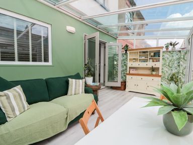 A sunroom with a green couch a white cabinet and plants at 41 Chatsworth Gardens Scarborough
