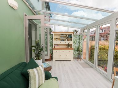 A conservatory with a green sofa white cabinet and glass roof at 41 Chatsworth Gardens in Scarborough