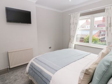 A bedroom with a bed covered with pillows and a blanket a wall mounted television radiator and a window with curtains at 41 Chatsworth Gardens in Scarborough