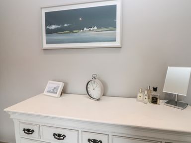 A white dresser with a clock small framed picture perfume bottles and a mirror on top at 41 Chatsworth Gardens in Scarborough