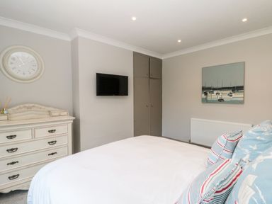 A bedroom with a bed with patterned pillows a wall clock a dresser a wall-mounted television and a painting at 41 Chatsworth Gardens in Scarborough