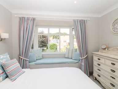 A bedroom with a bed with pillows a window seat with cushions curtains and a dresser with a clock on the wall at 41 Chatsworth Gardens in Scarborough