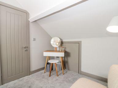 A small desk with a round mirror and stool in a room with slanted ceiling and closed doors at 41 Chatsworth Gardens in Scarborough