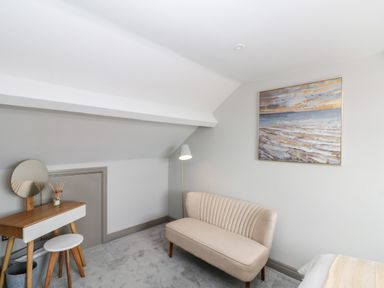 A room with a beige sofa a dressing table with mirror and stool a floor lamp and a painting on the wall at 41 Chatsworth Gardens in Scarborough