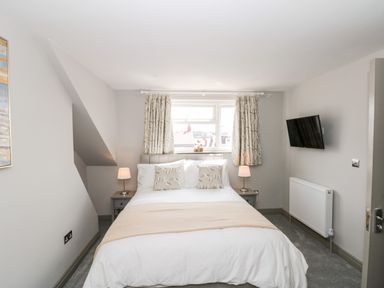 A bedroom with a bed two bedside tables with lamps curtains on the window and a wall-mounted television at 41 Chatsworth Gardens in Scarborough
