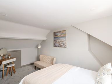 A bedroom with a bed a small sofa a floor lamp a dressing table with stool and a painting on the wall at 41 Chatsworth Gardens in Scarborough