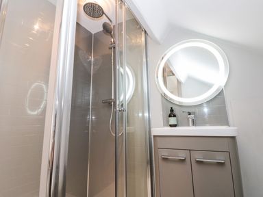 A bathroom with a glass shower enclosure a round illuminated mirror above a sink with a cabinet at 41 Chatsworth Gardens in Scarborough