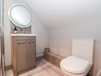 A bathroom with a sink and vanity unit with a round mirror above and a toilet at 41 Chatsworth Gardens in Scarborough
