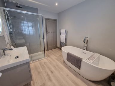 A bathroom with a white bathtub a gray towel a shower enclosure a sink a door and a towel rack at 41 Chatsworth Gardens in Scarborough