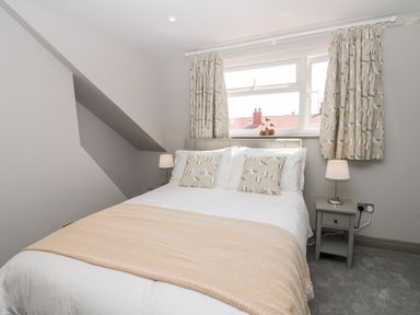 A bedroom with a double bed two bedside tables with lamps and a window with patterned curtains at 41 Chatsworth Gardens in Scarborough