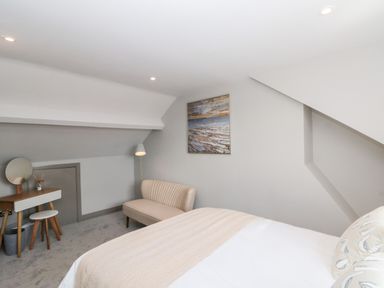 A bedroom with a bed a sofa a small vanity table with a stool and a floor lamp at 41 Chatsworth Gardens in Scarborough