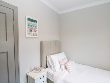 A bedroom with a bed with white bedding and striped pillows next to a white nightstand and a painting on the wall at 41 Chatsworth Gardens in Scarborough