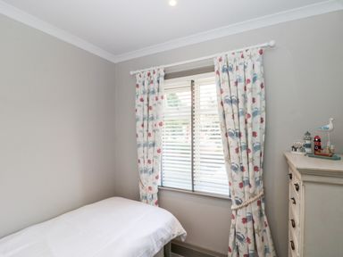 A bedroom with a bed white curtains with shell and crab patterns and a chest of drawers with decorative items at 41 Chatsworth Gardens in Scarborough