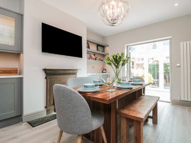 A dining room with a wooden table set with plates and bowls chairs a bench and a vase of flowers at 41 Chatsworth Gardens in Scarborough