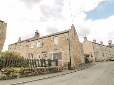 A street view of stone terraced houses with chimneys and a small front garden with a wooden fence at 4 Tyne View in Wark