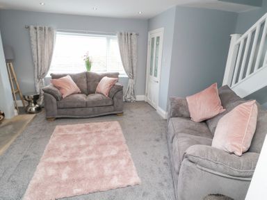 A living room with two grey sofas and pink cushions a pink rug on the floor and a window with curtains at 4 Tyne View in Wark