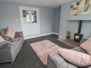 A living room with two sofas a pink rug a wood burning stove and double doors at 4 Tyne View in Wark