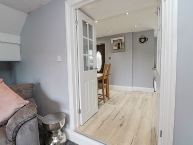 A room with a grey couch and side table leading to a dining area with wooden chairs at 4 Tyne View in Wark