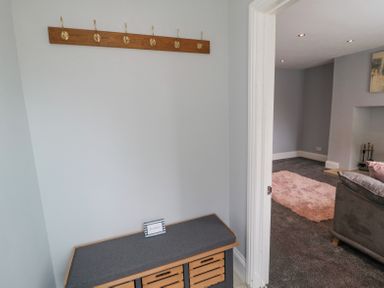 A hallway with a wooden coat rack above a cushioned bench connected to a living room with a gray carpet and a pink rug at 4 Tyne View in Wark